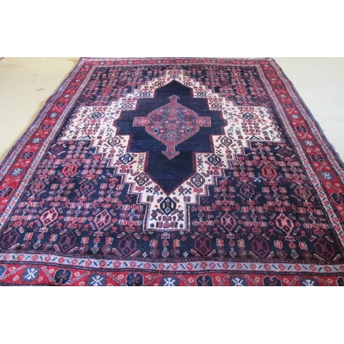 959 - An antique Persian Senneh rug with a deep rich central motif highlighted on a cream ground with styl... 