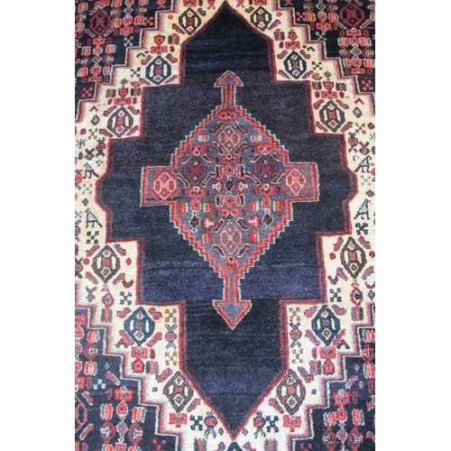 959 - An antique Persian Senneh rug with a deep rich central motif highlighted on a cream ground with styl... 