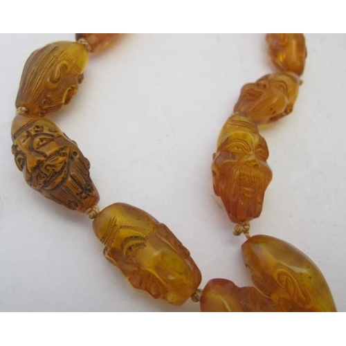 494 - A rare honey coloured amber figural face carved prayer necklace. Having eighteen carved face beads, ... 