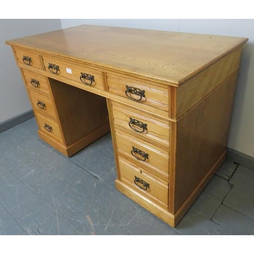 709 - An Edwardian light oak kneehole desk, housing an array of nine graduated drawers with brass drop han... 