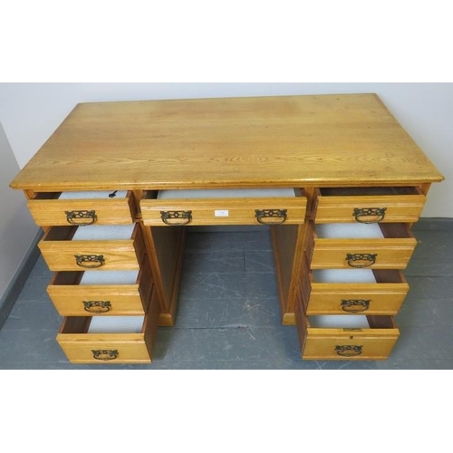 709 - An Edwardian light oak kneehole desk, housing an array of nine graduated drawers with brass drop han... 