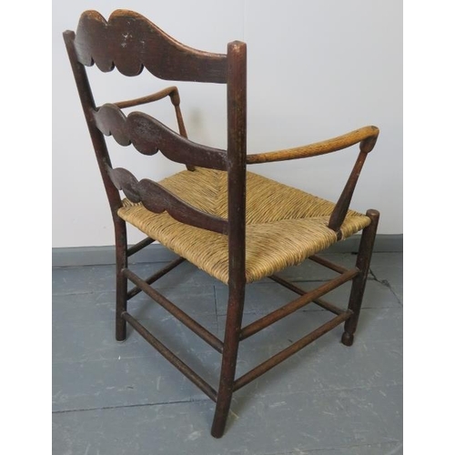 753 - A Georgian elm country made elbow chair, with shaped backrest and rush seat, on turned supports with... 