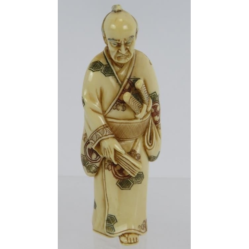 13 - A finely carved Japanese ivory Netsuke, Meiji period of a standing Samurai, decorated in red and bla... 