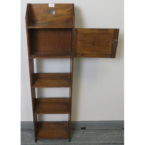 730 - An Arts & Crafts elm and oak narrow open bookcase of three shelves, with locking cupboard and pierce... 