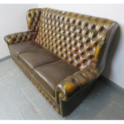 701 - A vintage three-seater chesterfield wingback sofa, upholstered in buttoned green leather with brass ... 