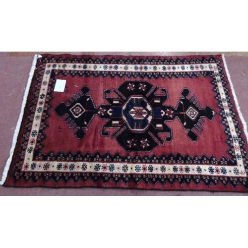 927 - A Persian rug on red ground with central blue/black motif. 150cm x100cm (approx).