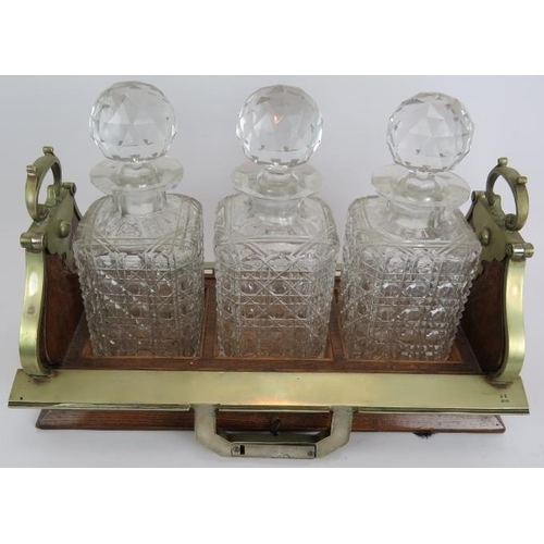 66 - An Edwardian oak 3 decanter tantalus with locking mechanism and nickel mounts. Each decanter hobnail... 