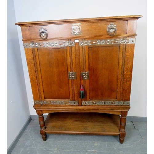 701 - An Arts & Crafts medium oak cabinet featuring ornate pierced steel escutcheons, drop ring handles an... 