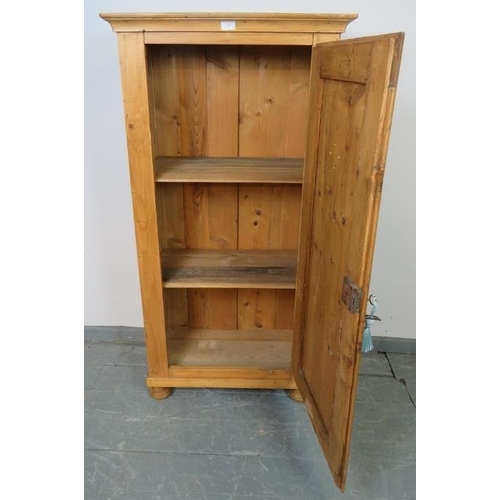 801 - An antique stripped pine pantry cupboard, housing three loose shelves, with panelled door, on bun fe... 