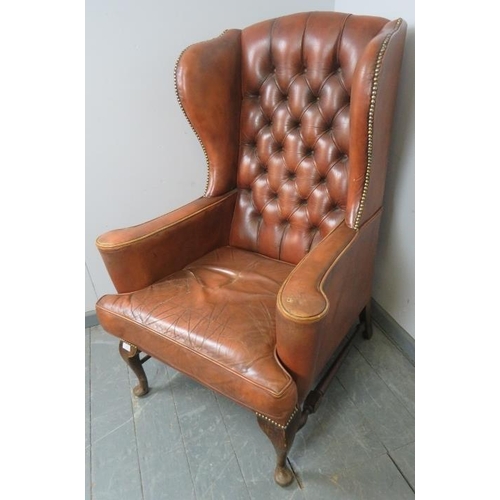 845 - A vintage wingback armchair in the Queen Anne taste, upholstered in deeply buttoned distressed tan l... 