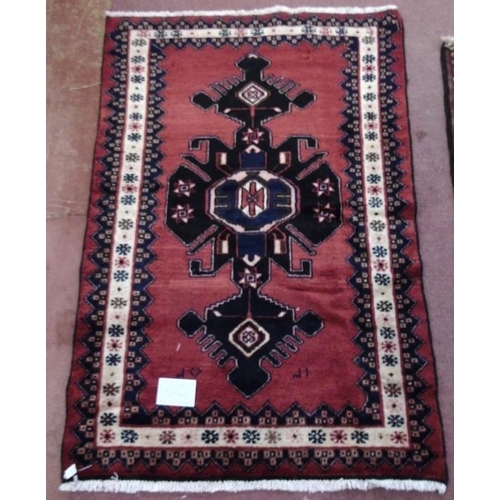 927 - A Persian rug on red ground with central blue/black motif. 150cm x100cm (approx).