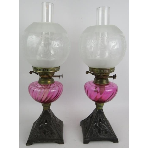 245 - A pair of antique oil lamps with cast iron bases decorated with birds, cranberry glass reservoirs an... 