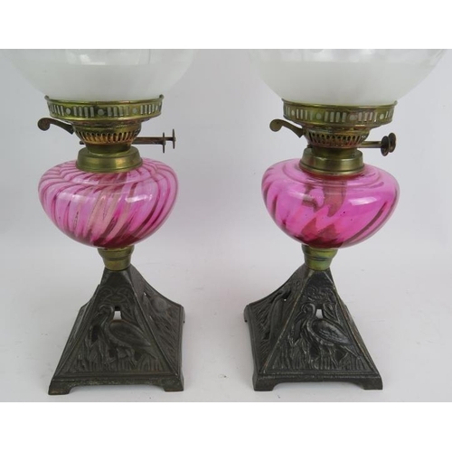 245 - A pair of antique oil lamps with cast iron bases decorated with birds, cranberry glass reservoirs an... 