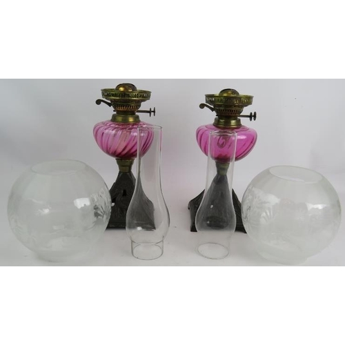 245 - A pair of antique oil lamps with cast iron bases decorated with birds, cranberry glass reservoirs an... 