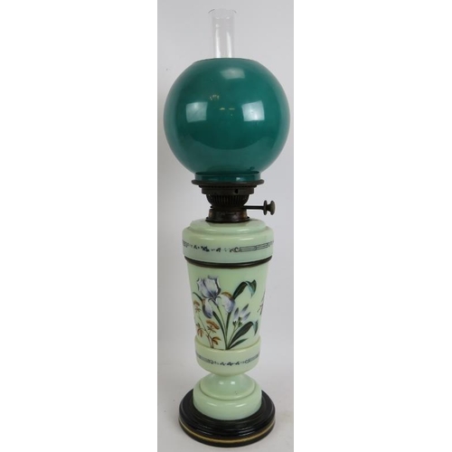 246 - An antique painted glass oil lamp hand decorated with flowers on a ceramic base and with green glass... 