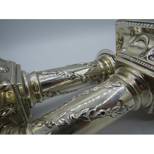 303 - A pair of Victorian silver candlesticks embossed with foliate design on the columns and rams head & ... 