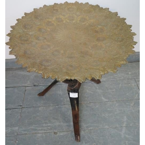 723 - An antique North African tray top table, the shaped and dished brass top intricately hand worked wit... 