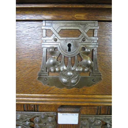 747 - An Arts & Crafts medium oak cabinet featuring ornate pierced steel escutcheons, drop ring handles an... 