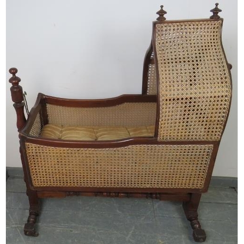 764 - A turn of the century mahogany rocking crib with turned finials and bergère sides and canopy, on a b... 