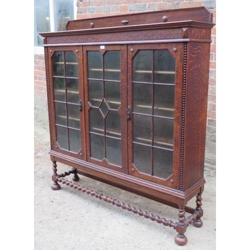 827 - A 1920s Jacobean Revival glazed bookcase featuring carved frieze, the tracery glazed doors opening o... 