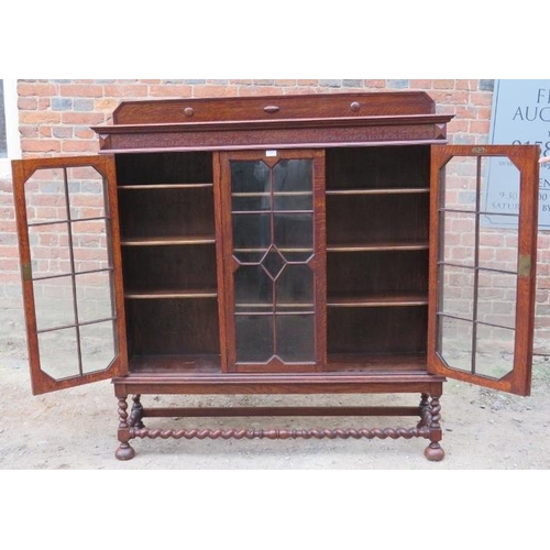 827 - A 1920s Jacobean Revival glazed bookcase featuring carved frieze, the tracery glazed doors opening o... 