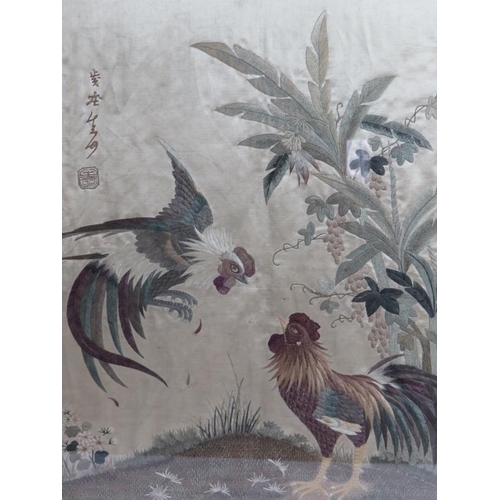 182 - An antique Chinese silk work panel depicting a pair of fighting cockerels with Chinese characters an... 