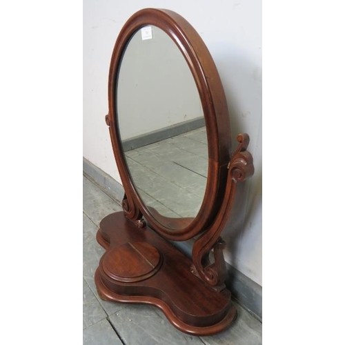 705 - A Victorian mahogany oval swing vanity mirror, with scrolled and pierced uprights, on a shaped plint... 