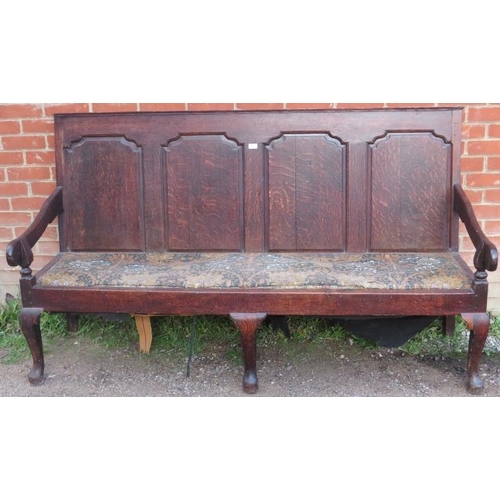 723 - An 18th century oak settle, the backrest with fielded panels, joined with open-sided armrests, on ca... 