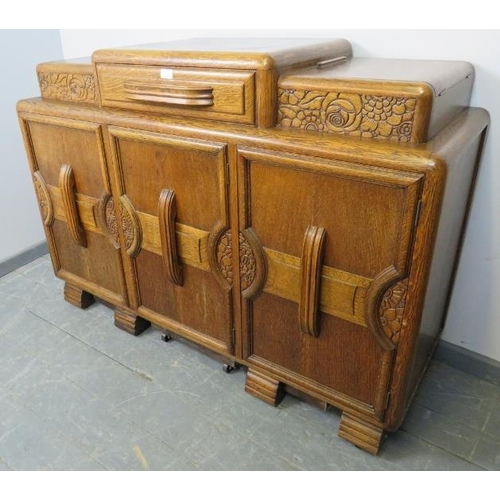 773 - An Art Deco medium oak sideboard, with central drawer flanked by lidded compartments, above three cu... 