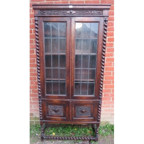 818 - A tall 1920s Jacobean Revival oak bookcase featuring barley twist uprights, the glazed doors with le... 