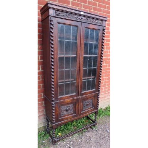 818 - A tall 1920s Jacobean Revival oak bookcase featuring barley twist uprights, the glazed doors with le... 