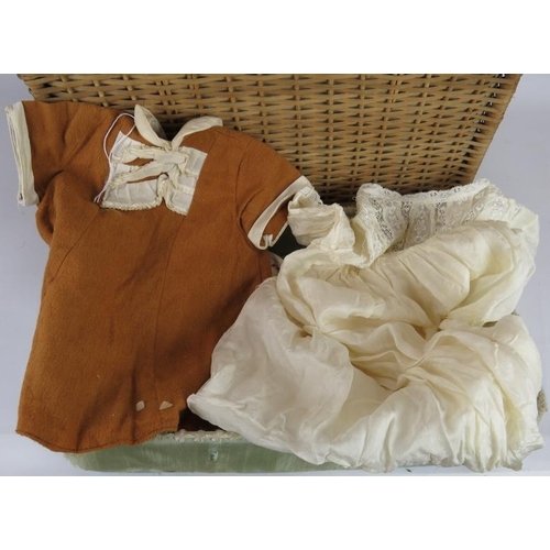 69 - A early 20th century silk lined basket with lift out tray containing 9 period dolls dresses and 6 it... 