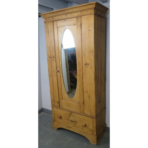 797 - An antique stripped pine single wardrobe, with hanging rail and hooks, the door with inset oval mirr... 