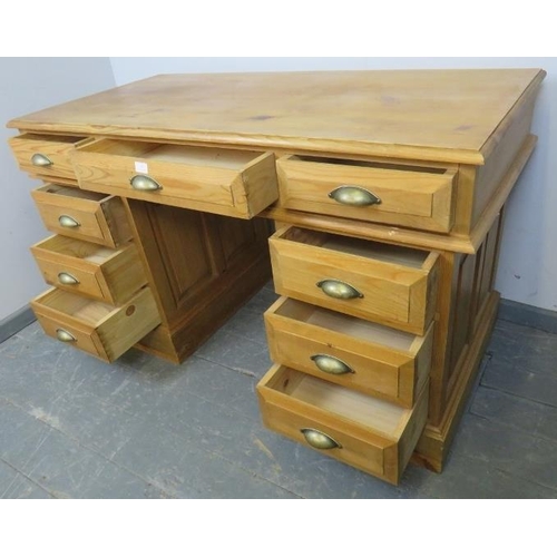 799 - A contemporary pine pedestal desk, featuring fielded panels, housing an array of nine drawers with b... 