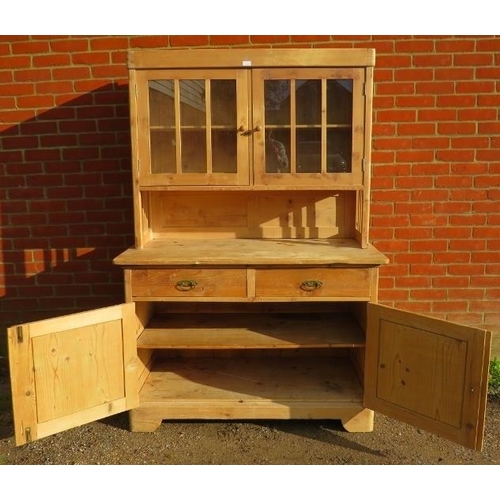 832 - An antique stripped pine kitchen dresser, the glazed doors opening onto one loose shelf, over a side... 