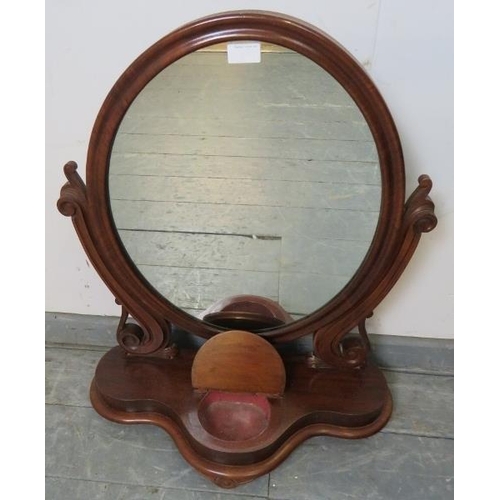 834 - A Victorian mahogany oval swing vanity mirror, with scrolled and pierced uprights, on a shaped plint... 