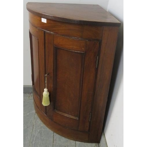 753 - A George III mahogany bow fronted wall-hanging corner cupboard, with reeded edge, the panelled doors... 