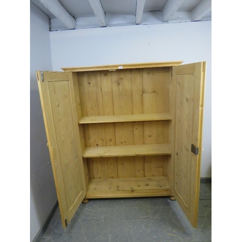 887 - An antique stripped pine pantry cupboard, the panelled doors opening onto two fitted shelves, on bun... 