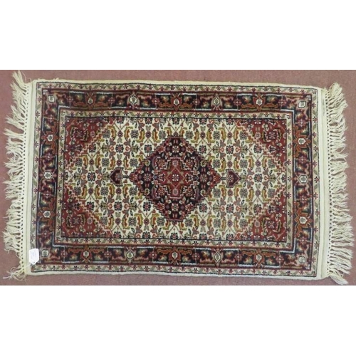 910 - Small Persian rug, central red motif on beige ground within blue and red border fringe. 103cm x 65cm... 