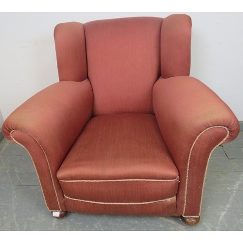 742 - An Edwardian wingback club armchair, re-upholstered in light burgundy material with silver braided r... 