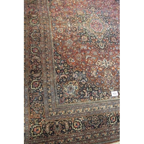 924 - A large Persian carpet c 1920's, central motif on pale red ground, with very wide blue/red/cream bor... 