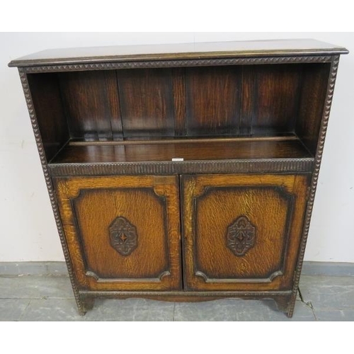 762 - A 1920s oak low bookcase with one open shelf above a chip carved frieze, over double doors with carv... 