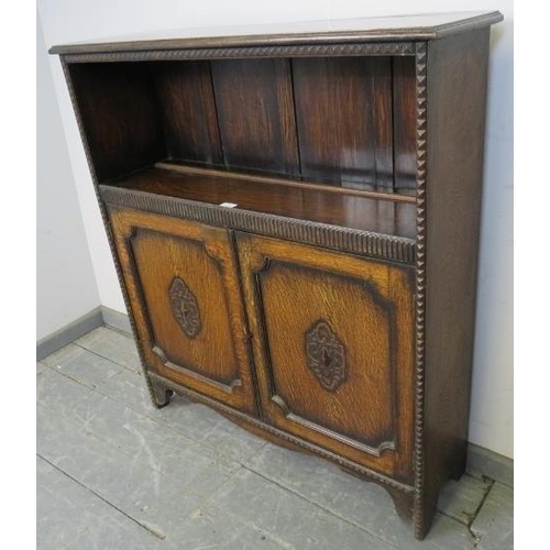 762 - A 1920s oak low bookcase with one open shelf above a chip carved frieze, over double doors with carv... 