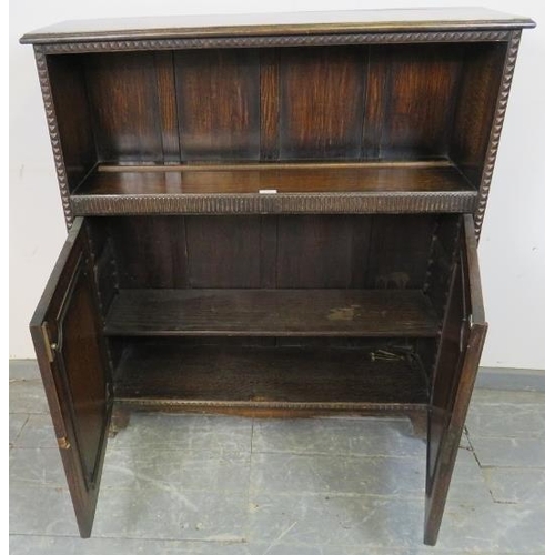 762 - A 1920s oak low bookcase with one open shelf above a chip carved frieze, over double doors with carv... 