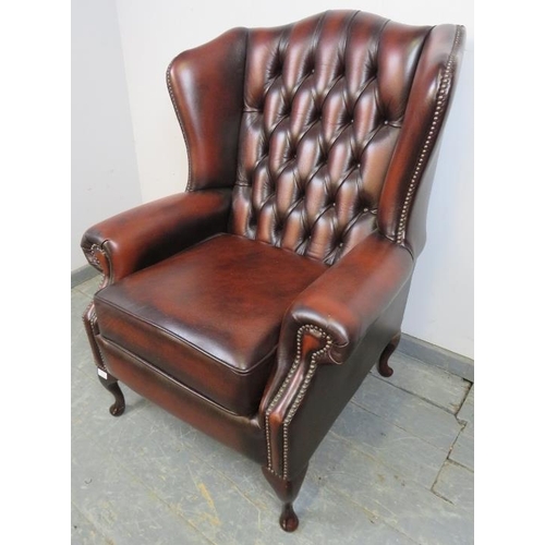 771 - A Queen Anne style wingback armchair, upholstered in buttoned burgundy leather with brass studs, on ... 