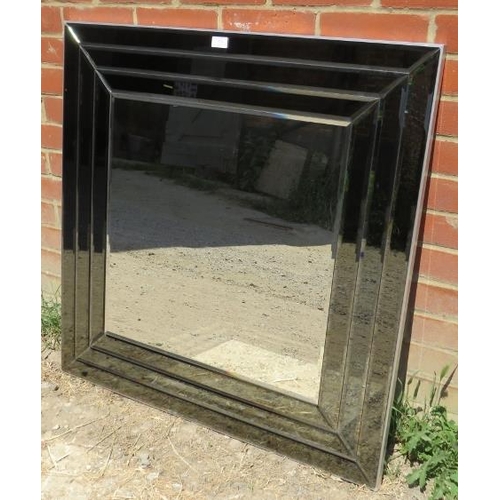 784 - A large square contemporary bevelled wall mirror, in a sectioned and bevelled smoked glass surround.... 