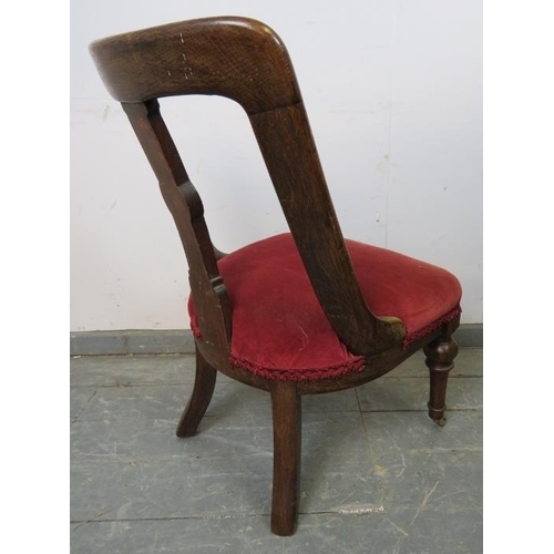 890 - An Arts & Crafts oak bedroom chair with rosette carved backsplat, upholstered in claret velvet, on t... 