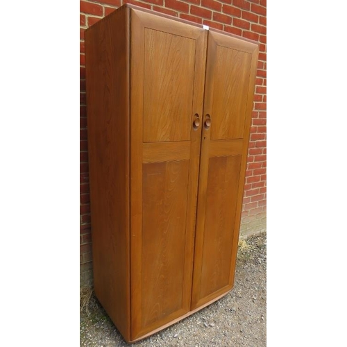 713 - A mid-century blonde elm Windsor double wardrobe by Ercol, the doors opening onto a hanging rail, ra... 