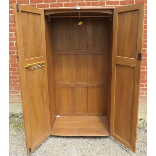 713 - A mid-century blonde elm Windsor double wardrobe by Ercol, the doors opening onto a hanging rail, ra... 