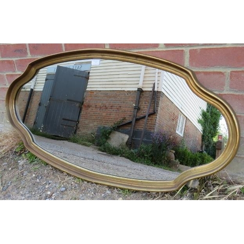 727 - A reproduction oval wall mirror in a shaped and dished gilt surround.
H54cm W111cm D4cm (approx).
Co... 